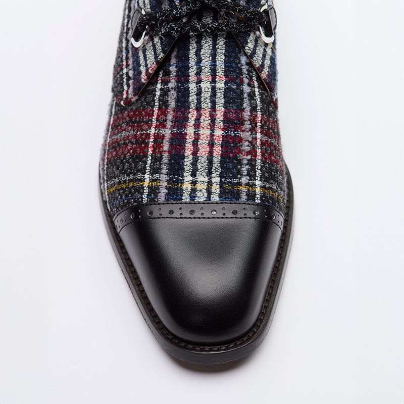 Detail of a men's lace-up shoe in checked tweed with brogued leather detail on the toe.