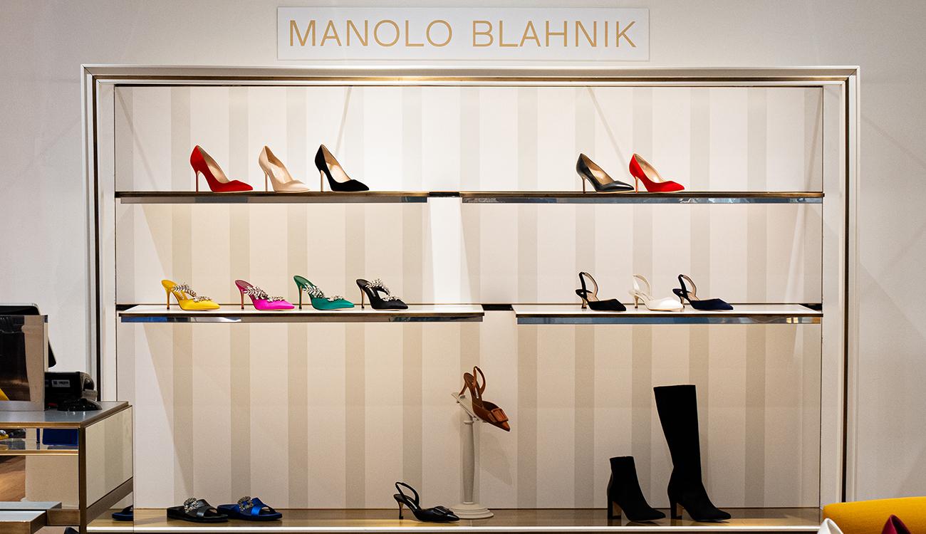 Image of the the interior of the store with a wall of various shoe styles and the Manolo Blahnik logo. 